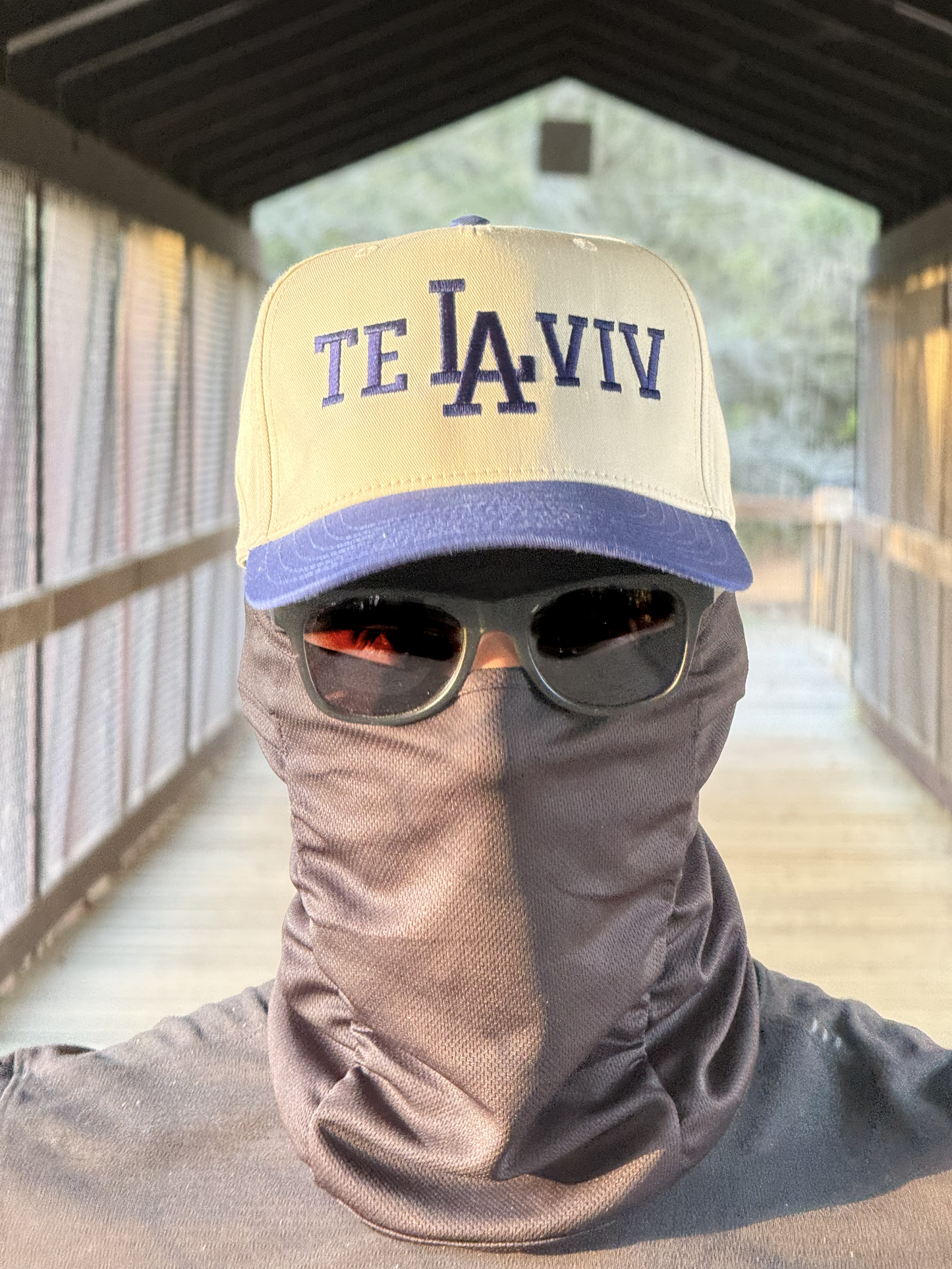A chud wearing a cap with 'TE LA VIV' text, sunglasses, and a balaclava in an outdoor setting.