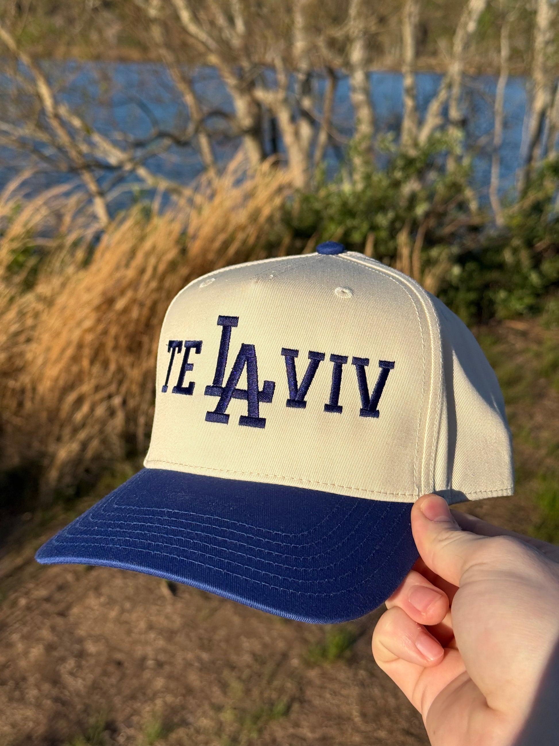Cap with 'TE LA IVIV' text held in front of a natural landscape